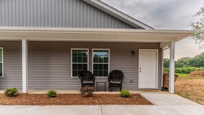 A two-story house with a covered porch, two chairs, a small table, and a door. - Near Atrium & town, King/Queen/Pullout, NO stairs (Lincolnton)