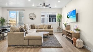 Un salon moderne avec un canapé d’angle, une table basse ronde et un téléviseur fixé au mur.