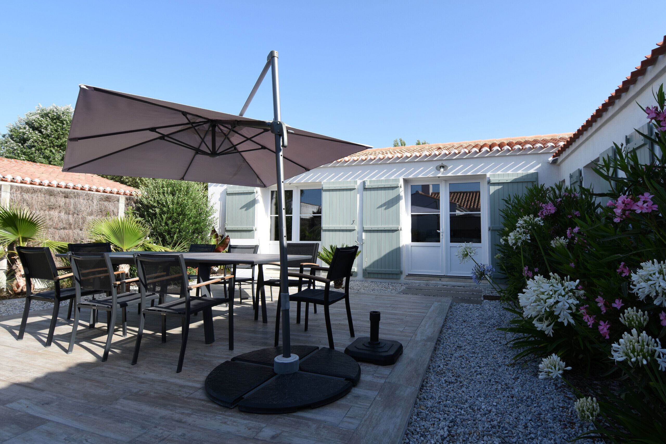 A patio with a table and chairs, a large umbrella, and a house with a tiled roof and windows.