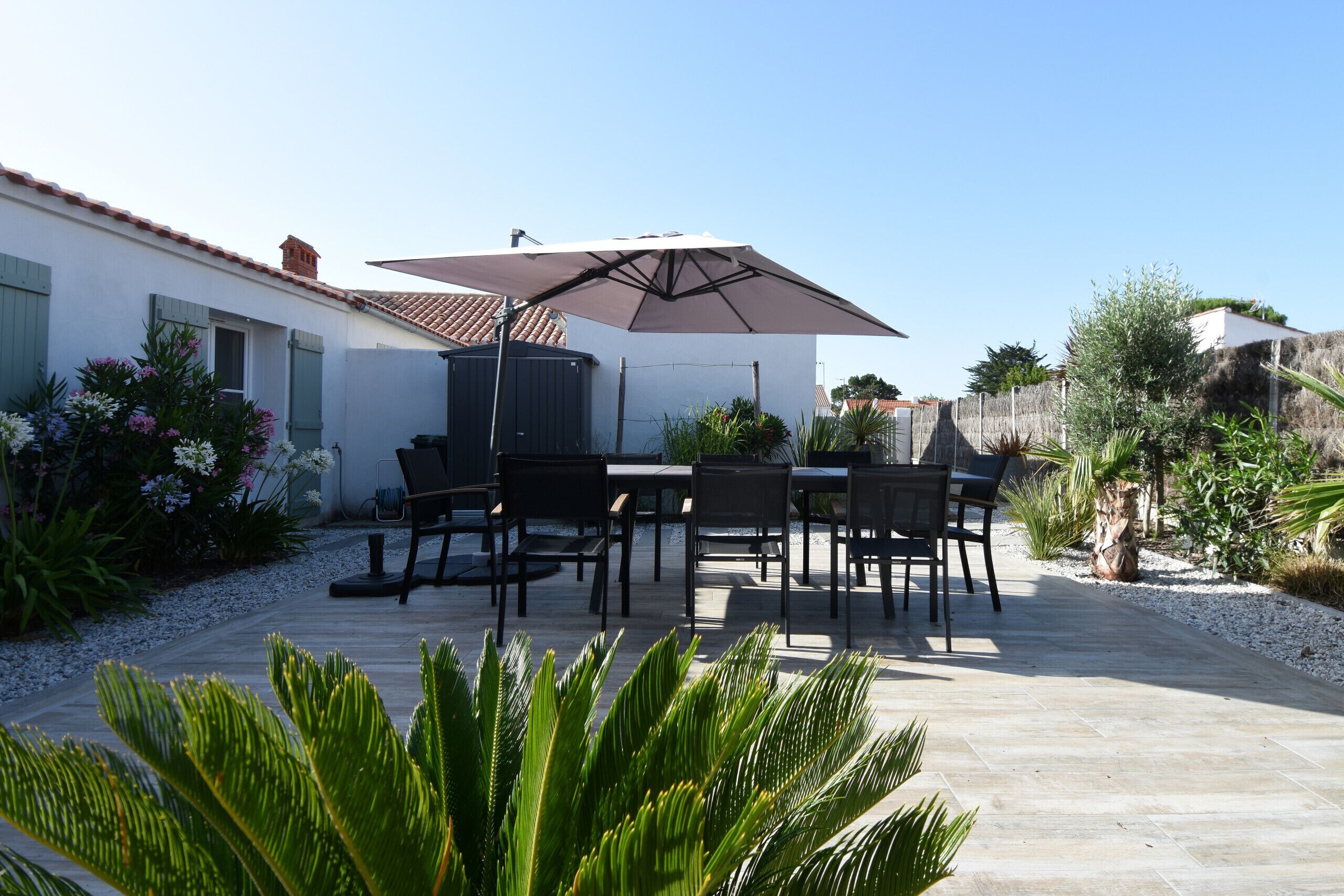 An outdoor patio with a table and chairs, a large umbrella, and various plants.