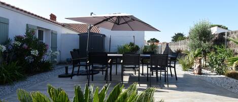 An outdoor patio with a table and chairs, a large umbrella, and various plants.