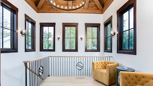 Une pièce spacieuse avec de grandes fenêtres, un plafond en bois et un escalier doté d’une rampe.