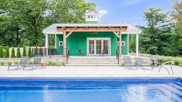 A poolside area with a green building, a covered seating area, and a clear blue pool.