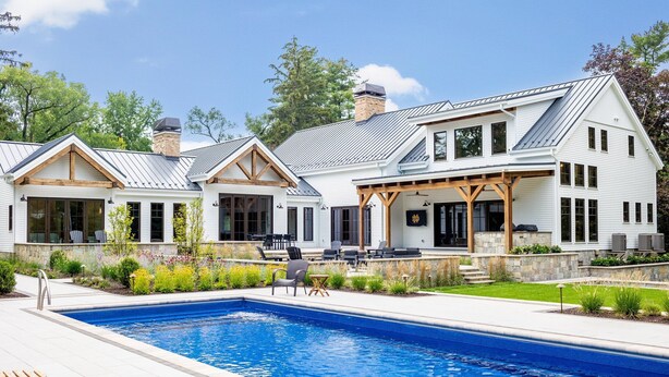 A two-story house with a large swimming pool, outdoor seating, and a covered patio area.