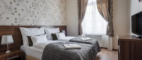 A hotel room with a bed, a bedside table with a lamp, a TV, and a window with curtains.