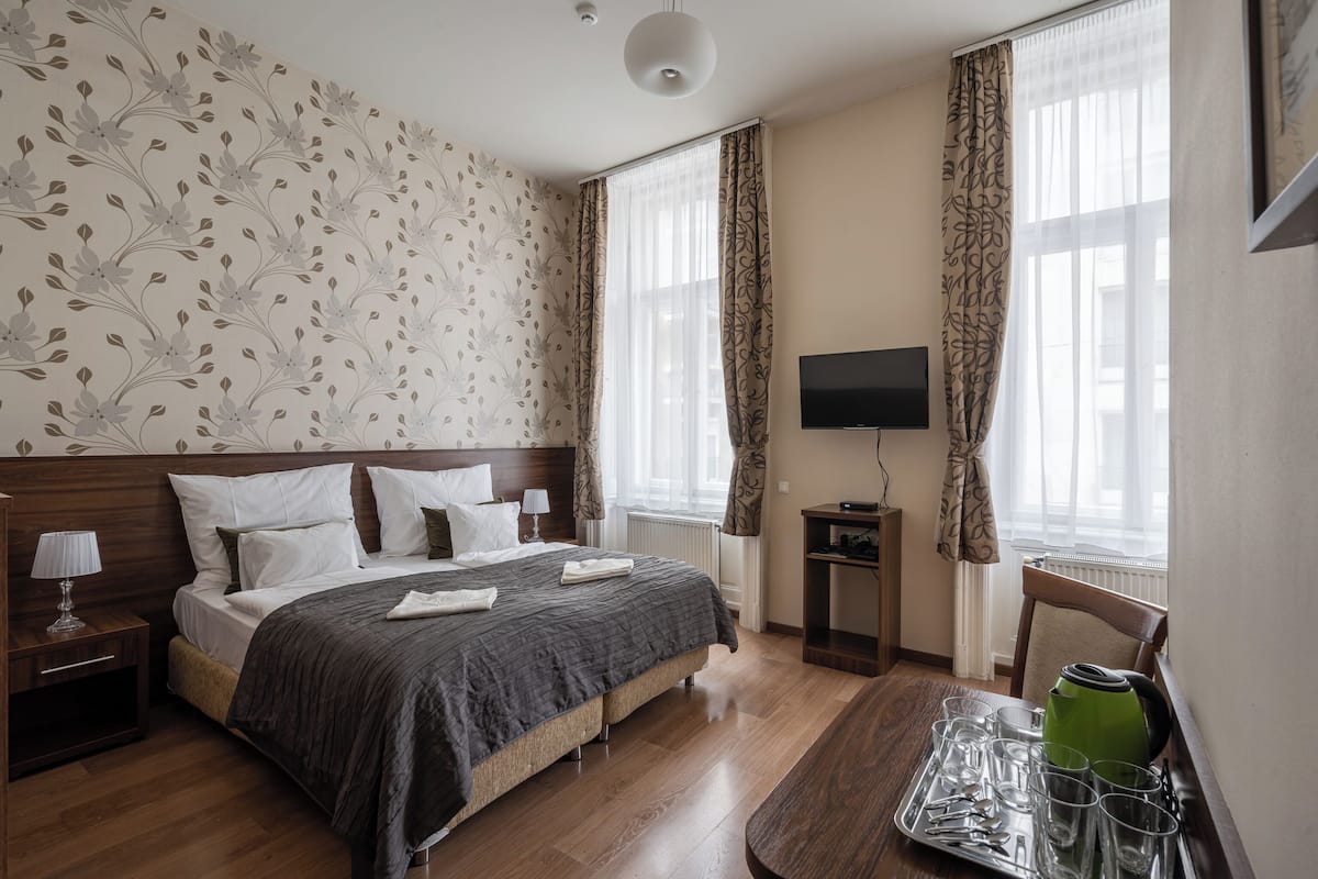 Une chambre d’hôtel équipée d’un lit, d’une table de chevet, d’une lampe, d’une télévision et d’un plateau avec des verres et une bouilloire.