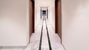 A long, narrow hallway with marble flooring and wooden doors on either side. - Treebo Kaveri (Nashik)