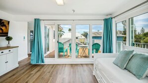 A room with a bed, a desk, and a view of a balcony with chairs and a table. - Beach Livin 5BR  Walk to Beach ~ Rooftop Deck ~3 Kitchens (Treasure Island)