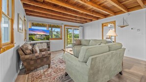 Un soggiorno ampio con soffitto in legno, una grande finestra vista panoramica, un divano verde, una poltrona marrone e un tappeto decorato.