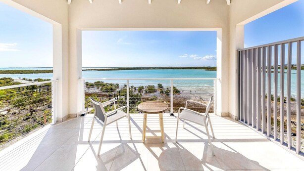 Ein Balkon mit Tisch und Stühlen, der Blick auf Strand und Meer gewährt.