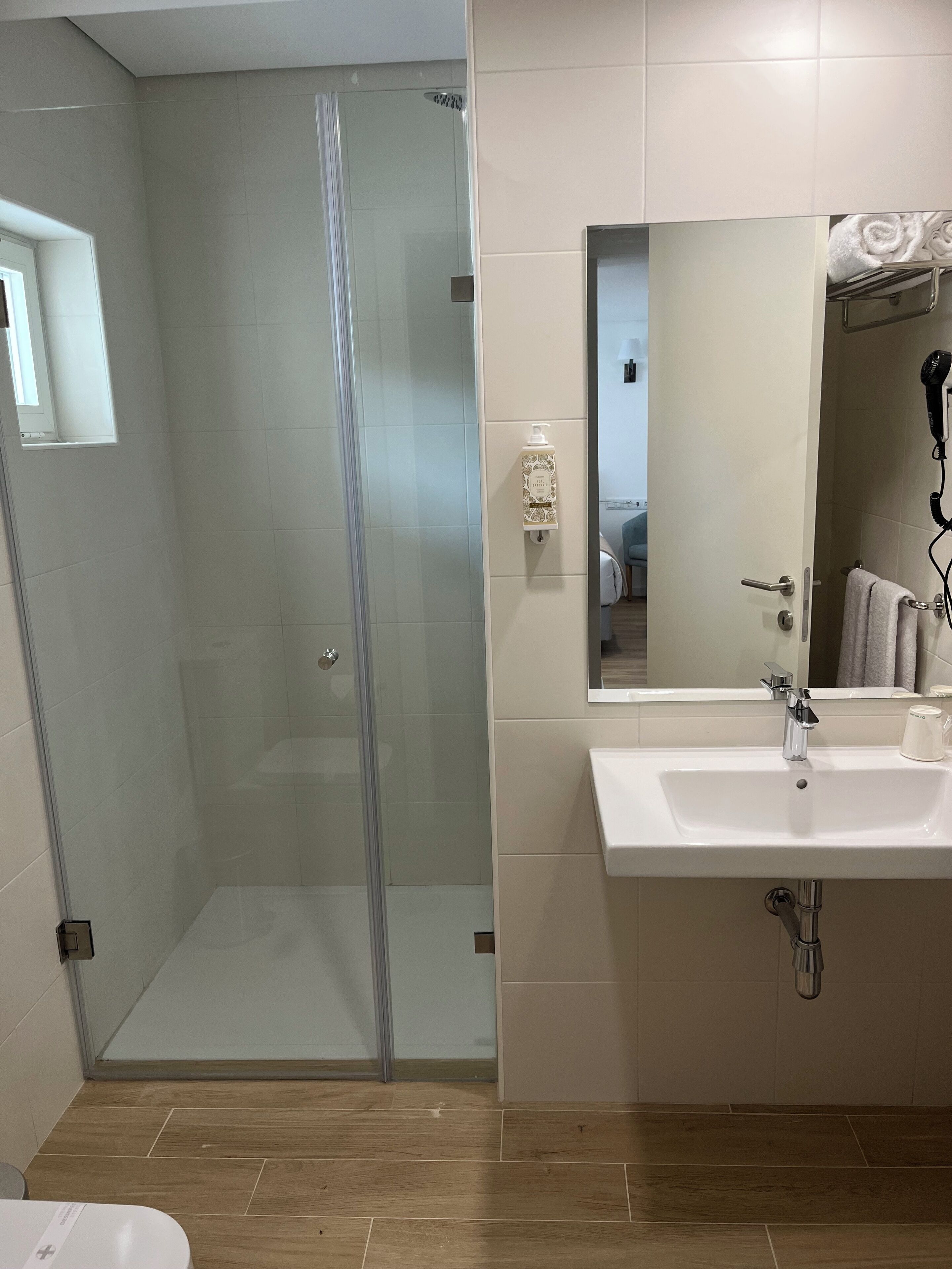 Un baño moderno con ducha de vidrio, un lavabo blanco con espejo y un secador de pelo en la pared.