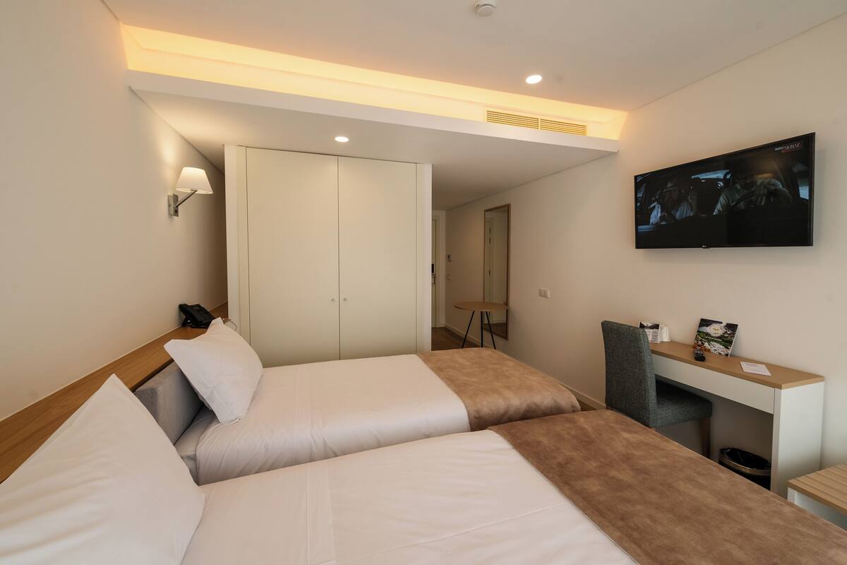 Ein Hotelzimmer mit zwei Betten, einem Schreibtisch, einem Fernseher und einem Kleiderschrank.