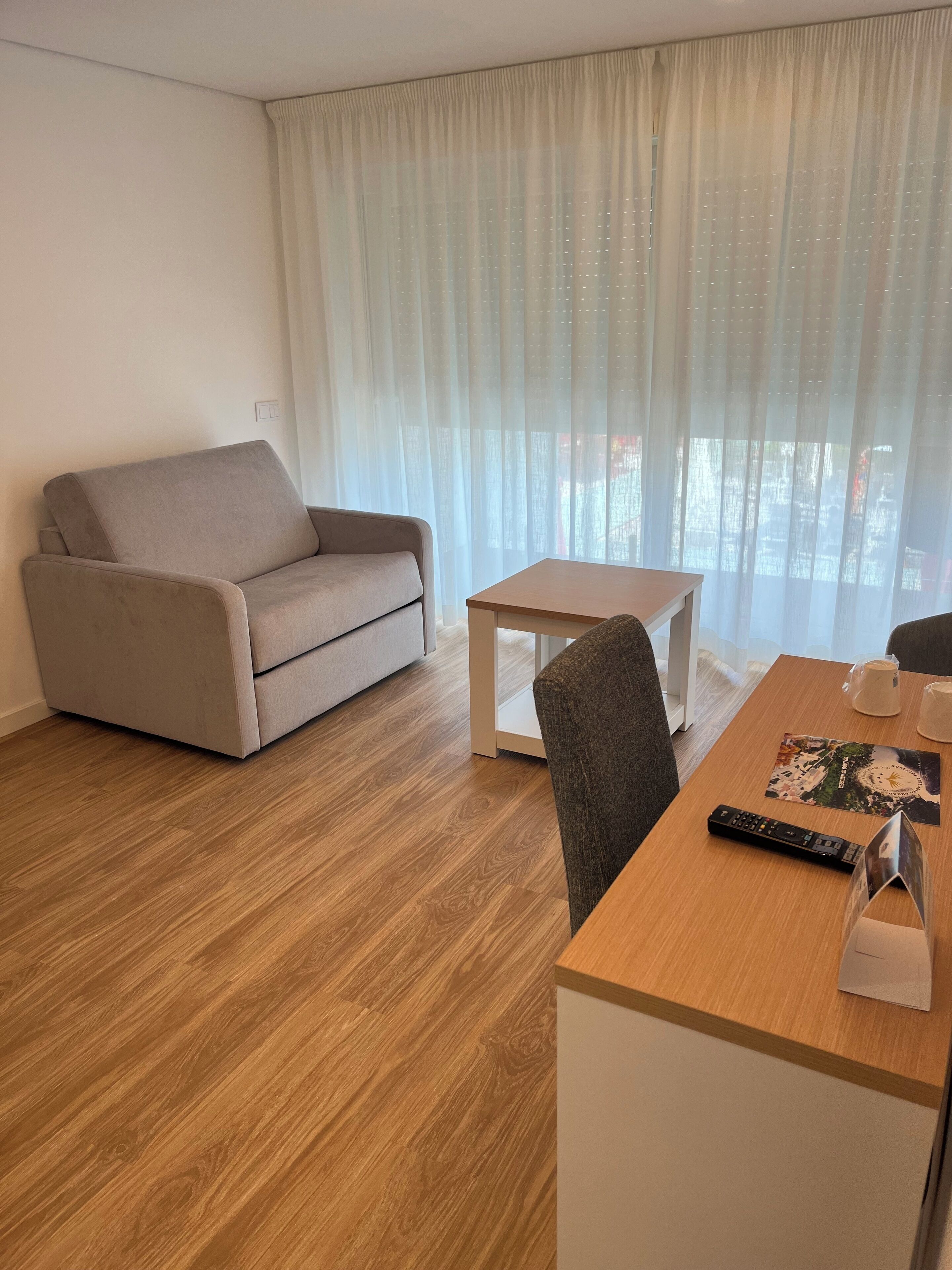 A modern living room with a beige sofa, a wooden coffee table, and a dining table with a remote control and a menu.