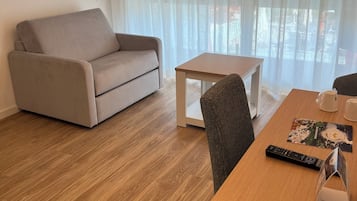 A modern living room with a beige sofa, a wooden coffee table, and a dining table with a remote control and a menu.