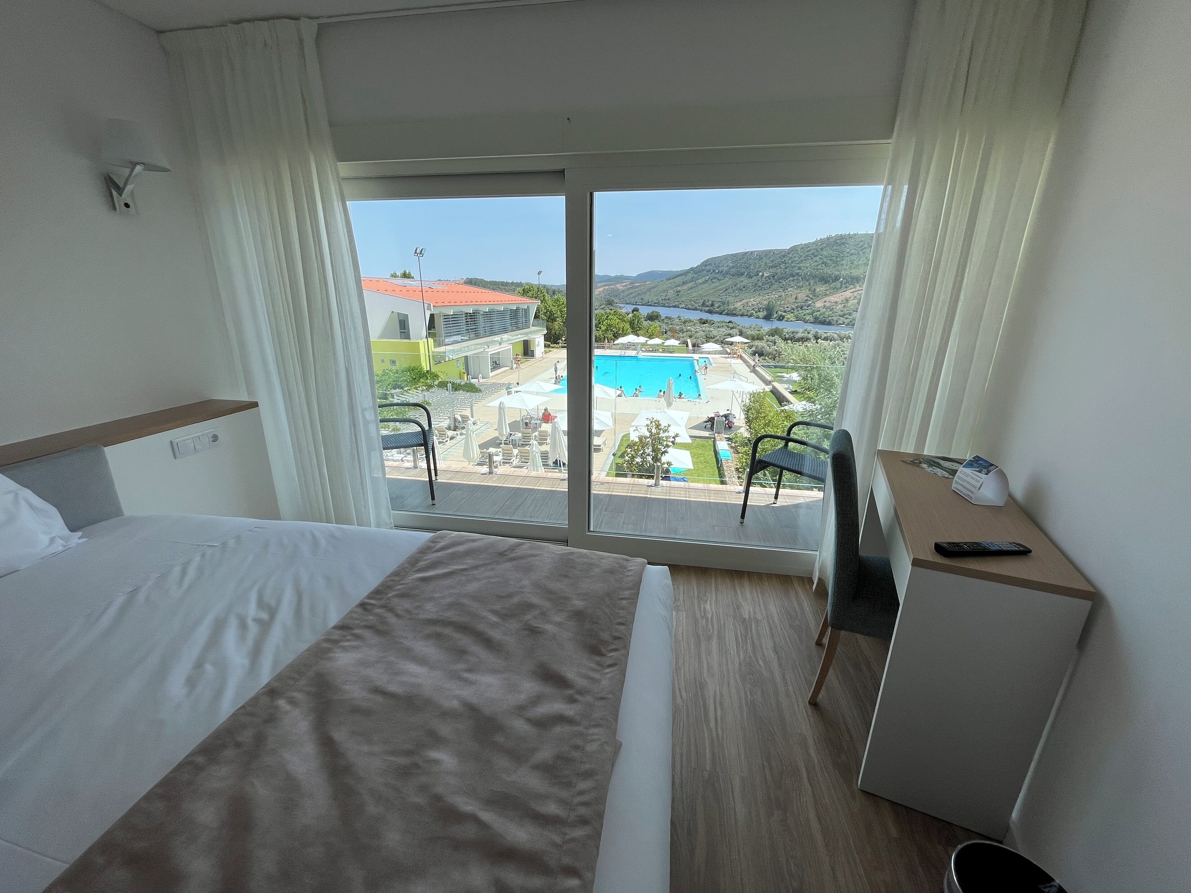 Une chambre d’hôtel avec un lit, un bureau et une vue sur une piscine et des immeubles.
