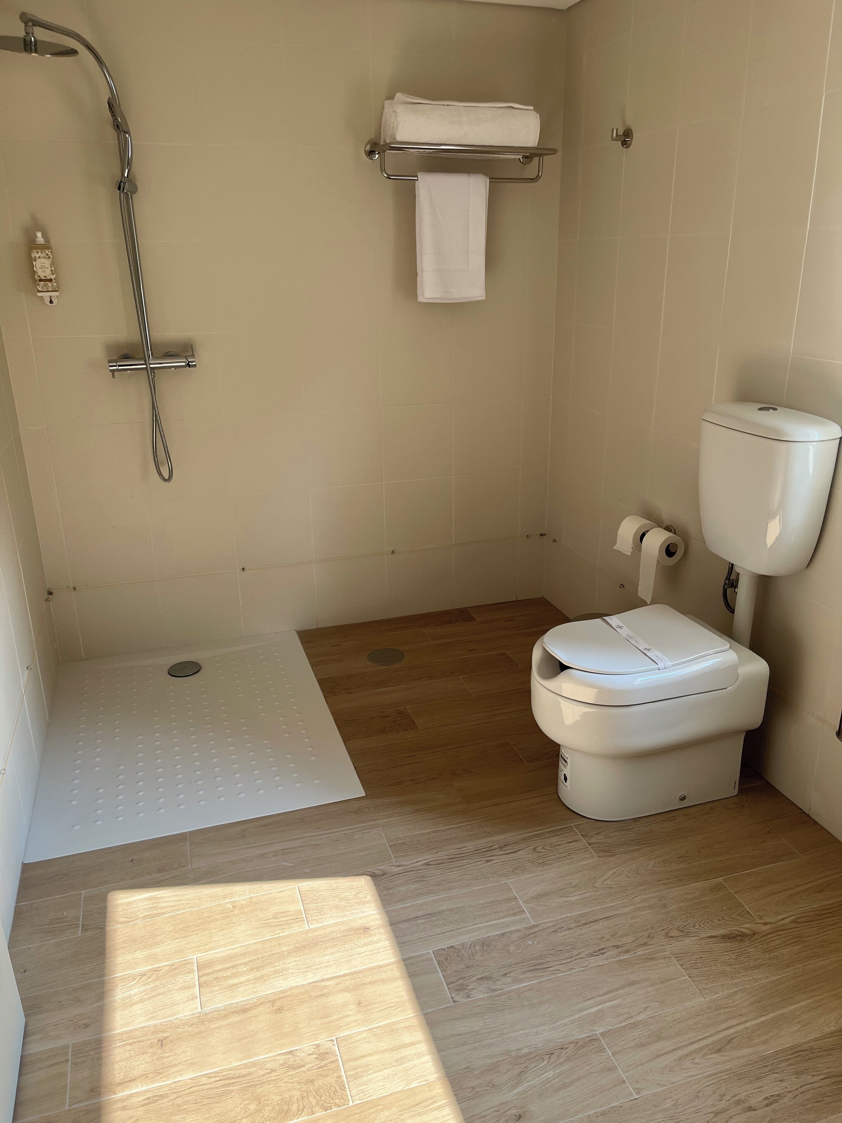 Une petite salle de bain avec une douche, des toilettes et une étagère sur laquelle est posée une serviette.