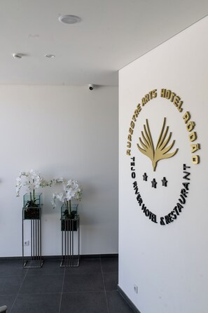 Ein Hotel-Rezeptionsbereich mit modernem Design, inklusive eines Logos an der Wand und zwei weißen Orchideen im Blumentopf.