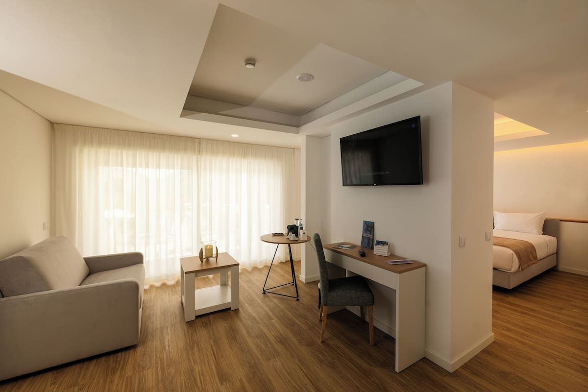 Ein modernes Hotelzimmer mit Sofa, Schreibtisch, Fernseher und Bett.