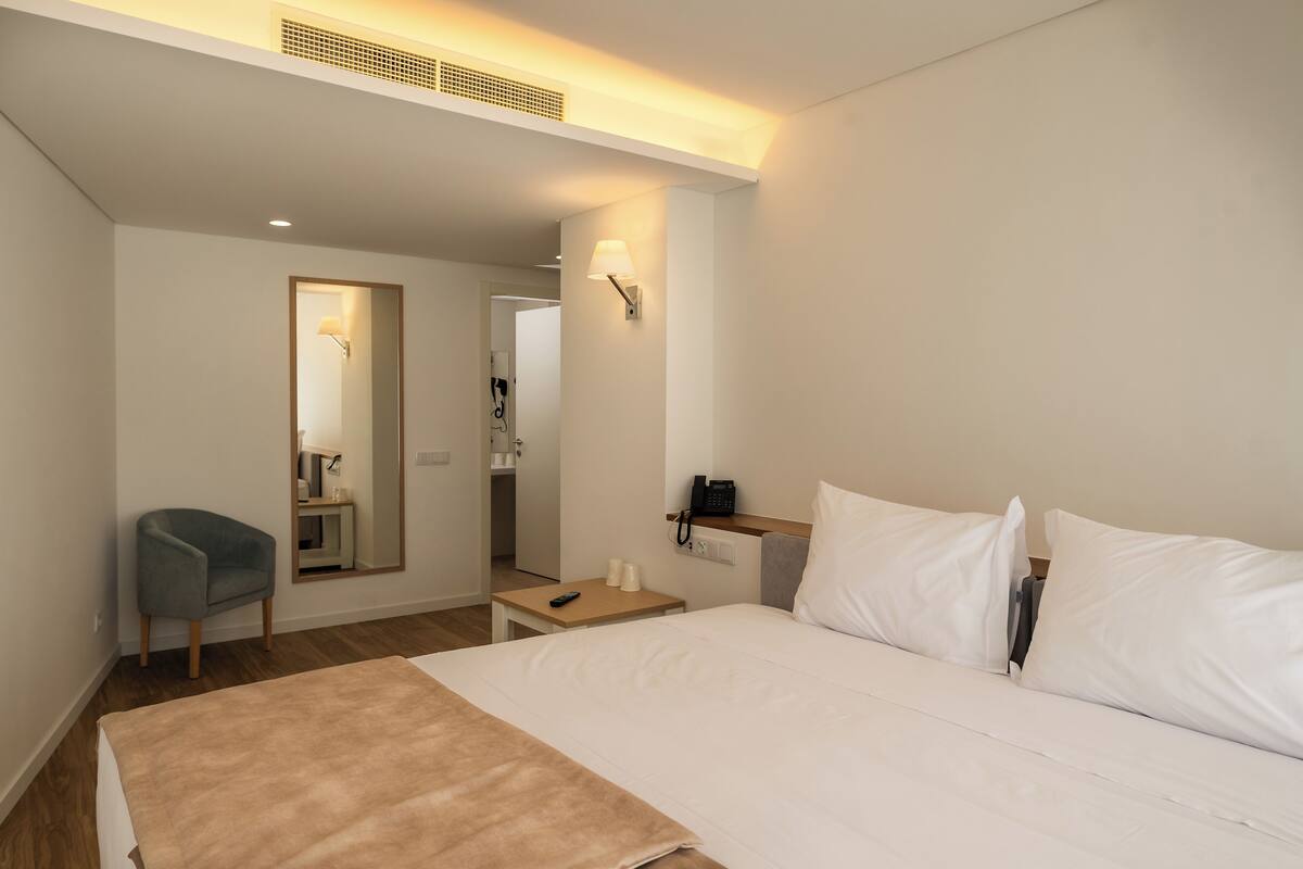 Ein Hotelzimmer mit einem Bett, einem Sessel, einem Schreibtisch mit Telefon und einem Spiegel.