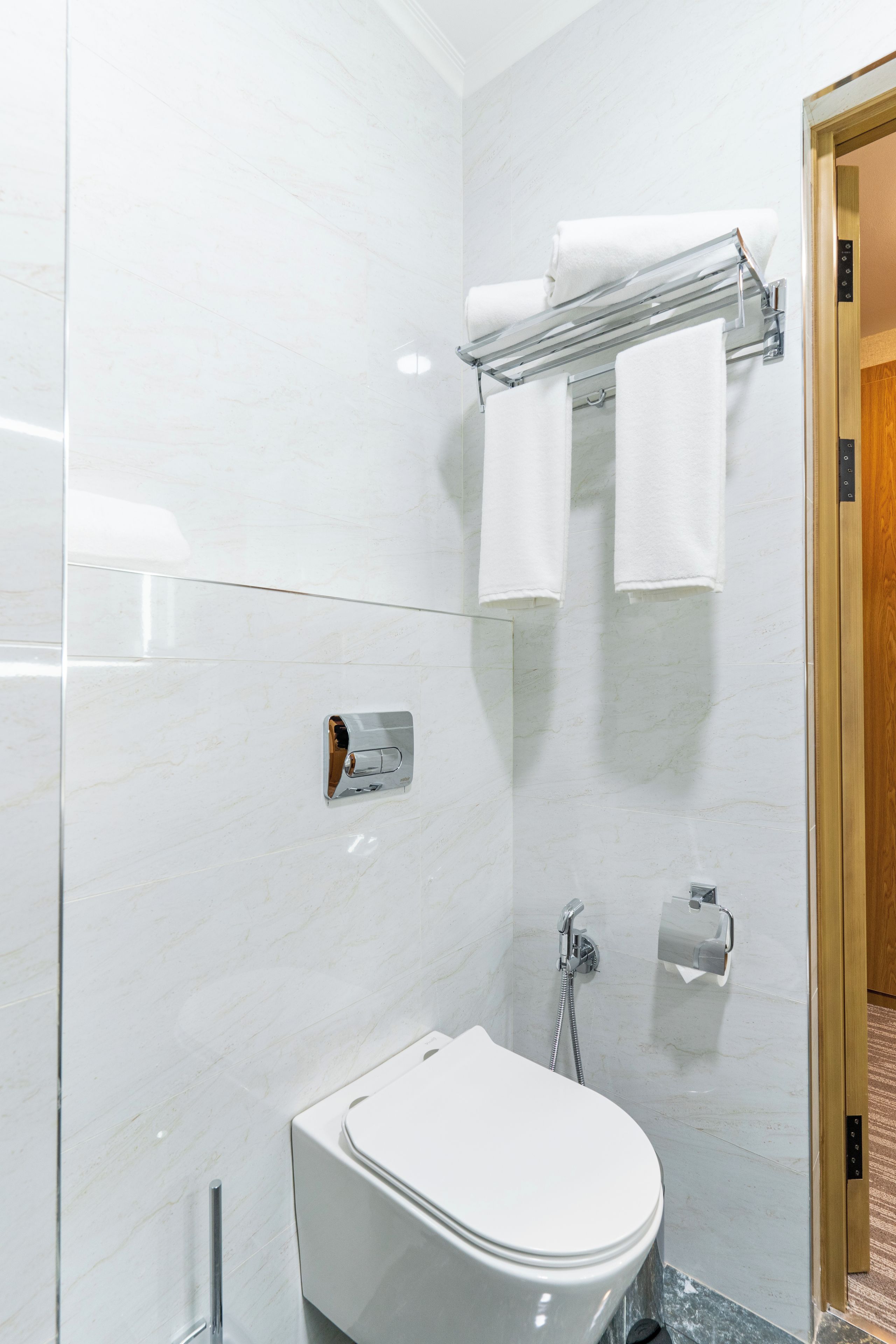 Een moderne badkamer met toilet, handdoekhouder, douche en toiletrolhouder.
