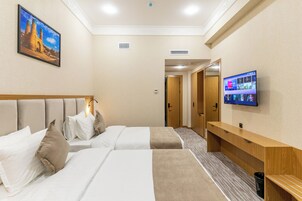 Habitación de hotel con dos camas, televisión, banca de madera y un cuadro en la pared.