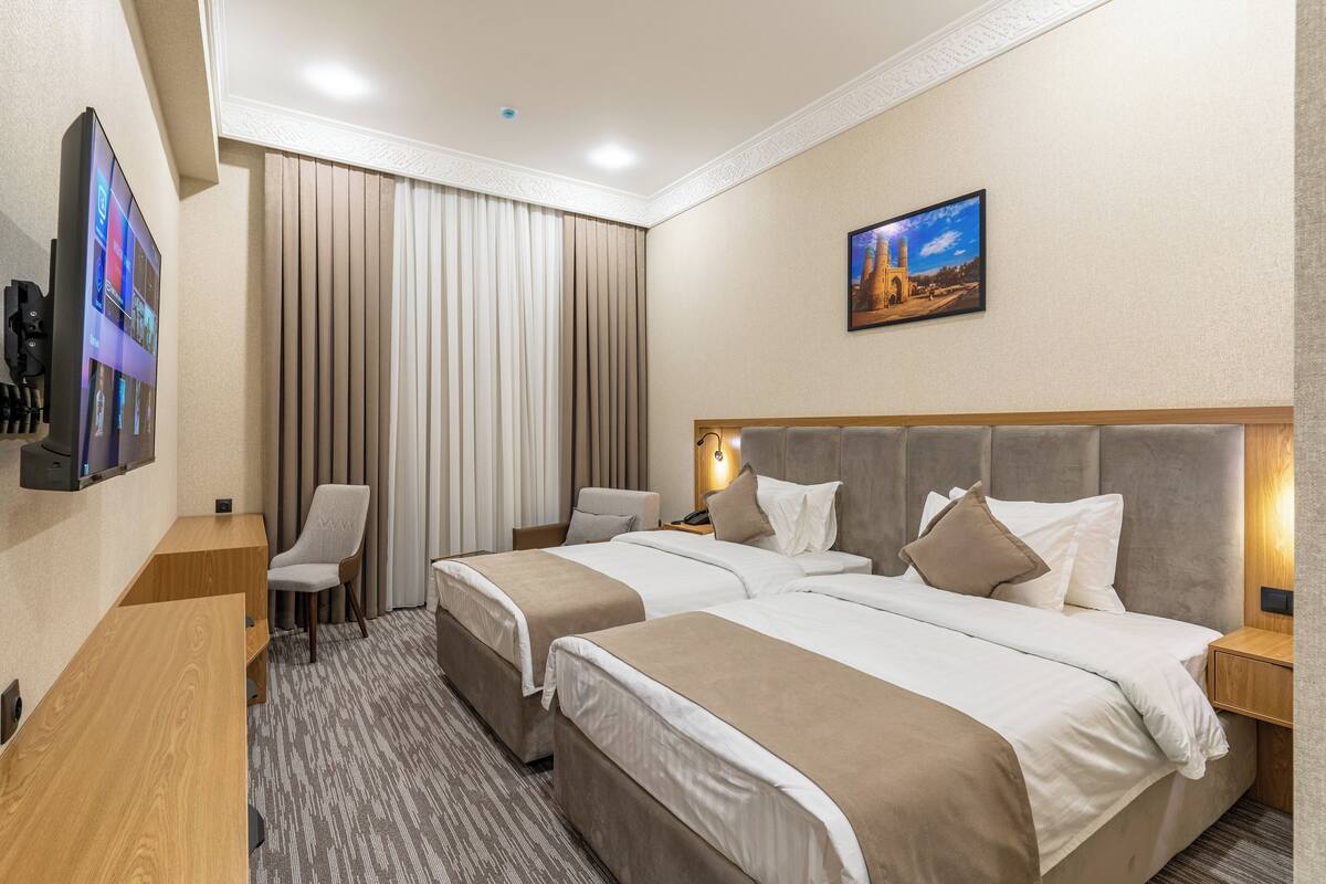 A hotel room with two beds, a desk, a chair, a TV, and a painting on the wall.
