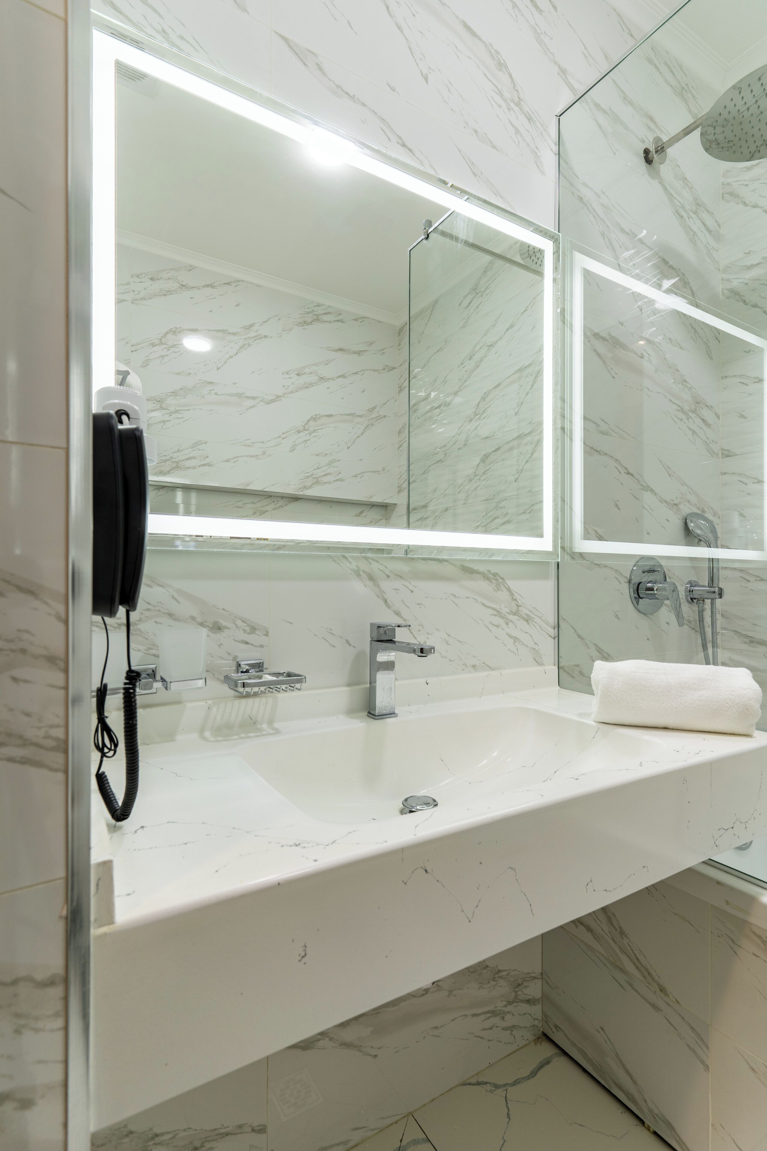 A modern bathroom with a marble sink, a glass shower enclosure, and a telephone.