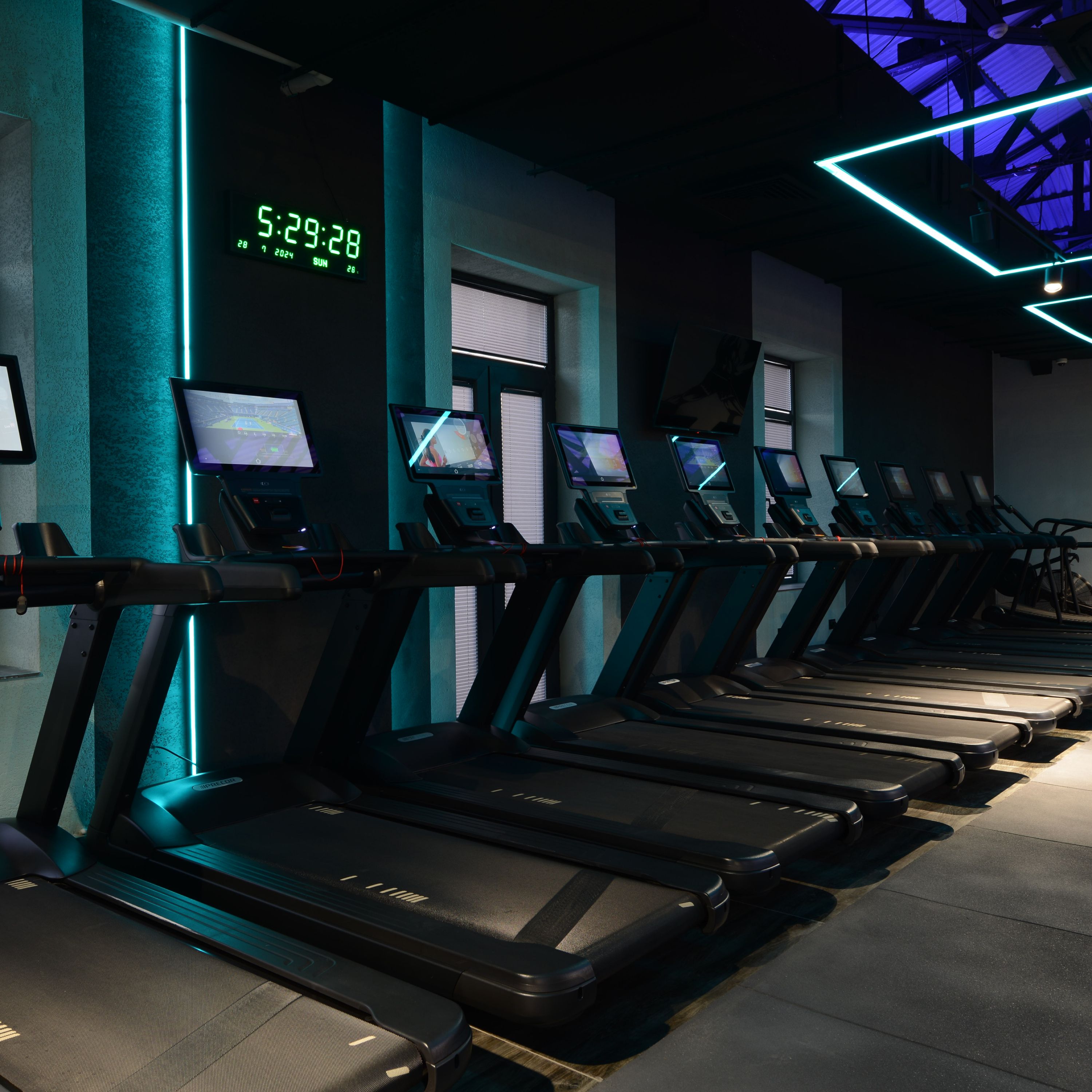 Un gimnasio con cintas de correr, pantallas digitales y un reloj que muestra la hora.