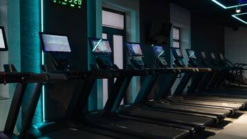 Un gimnasio con cintas de correr, pantallas digitales y un reloj que muestra la hora.
