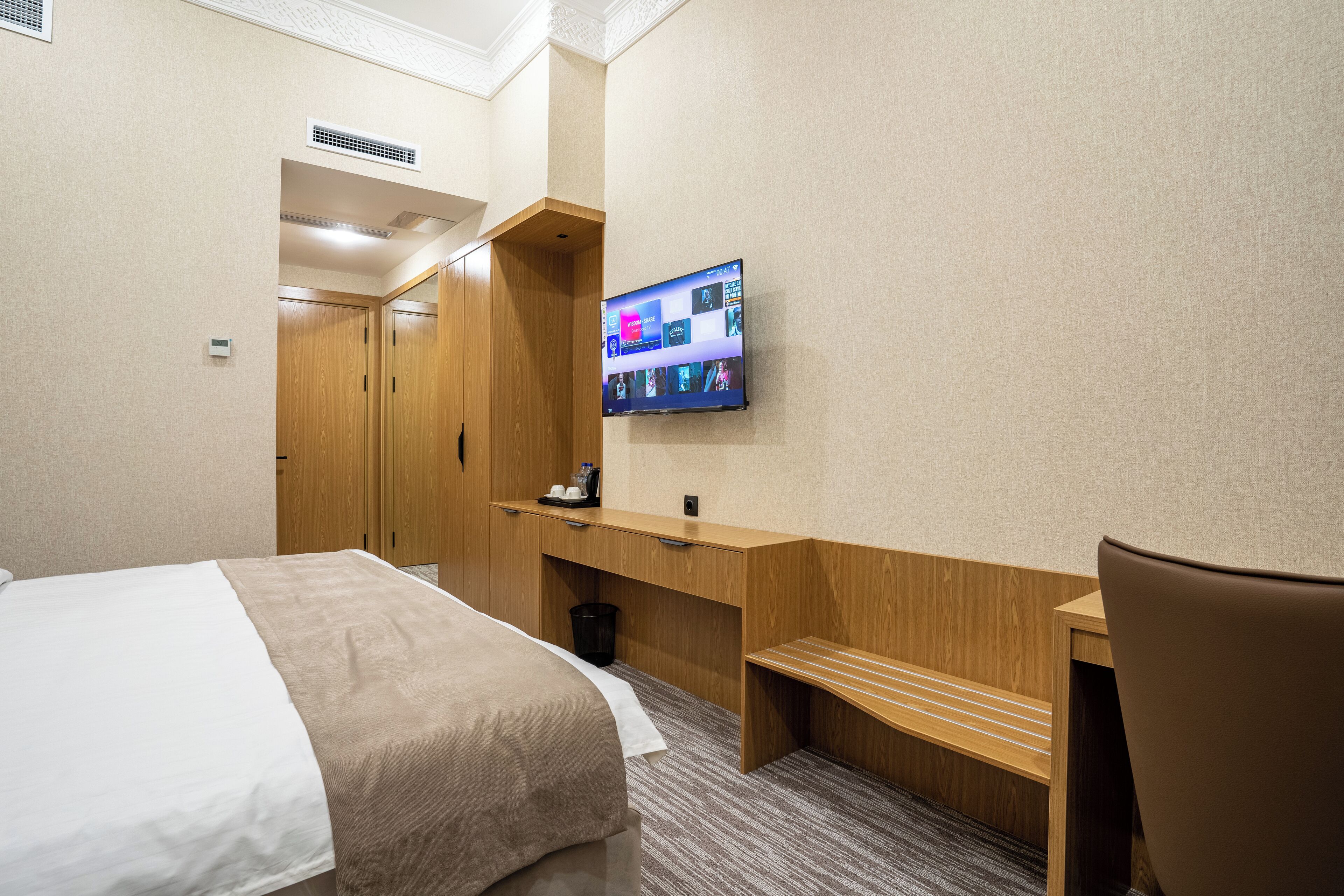 Ein Hotelzimmer mit einem Bett, einem Holztisch, einem an der Wand befestigten Fernseher und einem Sessel.