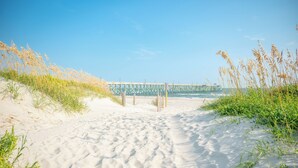 A sandy beach with a wooden pier in the background. - Lighthouse: Oceanfront with Pool and Elevator Near Fishing Pier (Oak Island)