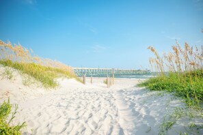 A sandy beach with a wooden pier in the background. - Lighthouse: Oceanfront with Pool and Elevator Near Fishing Pier (Oak Island)