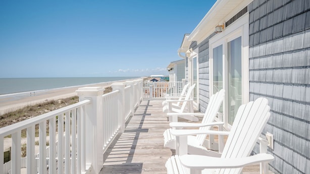 A wooden deck with white railings and chairs, overlooking a beach. - Lighthouse: Oceanfront with Pool and Elevator Near Fishing Pier (Oak Island)