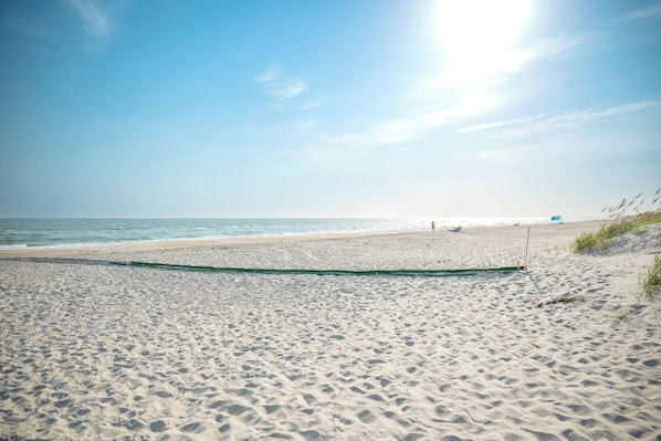A sandy beach with a clear sky and calm sea. - Lighthouse: Oceanfront with Pool and Elevator Near Fishing Pier (Oak Island)