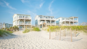 A beachfront property with multiple-story buildings, a sandy beach, and a wooden fence. - Lighthouse: Oceanfront with Pool and Elevator Near Fishing Pier (Oak Island)