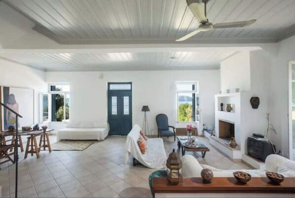 A spacious living room with a high ceiling, a fireplace, and a dining area with stools.