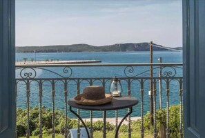 A balcony with a view of a body of water, a distant bridge, and a small table with a hat and lantern.
