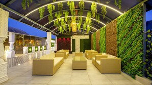 An outdoor seating area with wicker furniture, a green wall with plants, and a ceiling with hanging greenery. - Treebo Premium Embassy Inn (Noida)