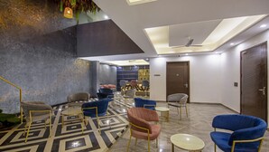 A modern lobby with geometric patterned flooring, a variety of seating options including armchairs and sofas, and a reception area with a wooden counter and bar sign. - Treebo Premium Embassy Inn (Noida)