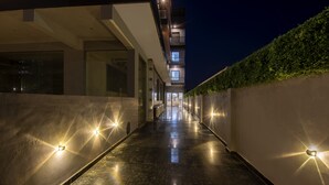 A modern building with a reflective floor, a glass entrance, and a green hedge along the side. - Treebo Premium Embassy Inn (Noida)