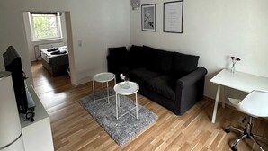 Ett modernt vardagsrum med en svart soffa, två vita sidobord, ett vitt skrivbord och en hängande lampa.
