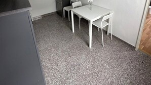 Ett litet, kompakt rum med ett pentry, ett vitt bord med två stolar, en vit lampa och en skylt med texten ”MITT HÄRLIGA STÄLLE”.