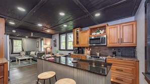 Une cuisine moderne avec des meubles en bois, un grand îlot central doté de tabourets et un coin repas comprenant un canapé et une table basse.