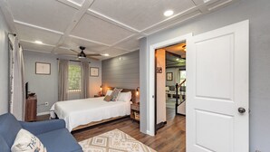 Une chambre à coucher avec un lit, un canapé bleu, un tapis à motifs et une porte blanche donnant sur une salle de bain.