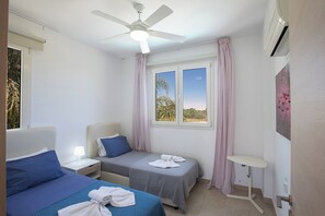 A hotel room with two beds, a ceiling fan, a window with curtains, and a small table.