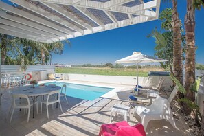 An outdoor pool area with a covered patio, lounge chairs, and a table with chairs.