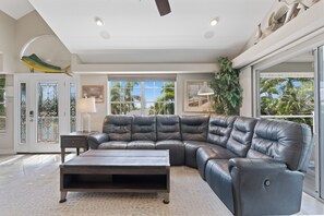 A spacious living room with a large L-shaped leather sofa, a wooden coffee table, and a view of palm trees through large windows. - 🛥️Canal Front with Boat Dock-Awesome Interior-The Sanctuary🛥️ (Fort Myers Beach)