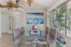 Un comedor moderno con una mesa de vidrio, sillas marrones y un cuadro de un paisaje tropical.