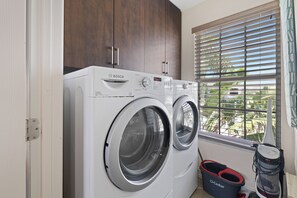 A Bosch washing machine in a laundry room with a view of palm trees through the window. - 🛥️Canal Front with Boat Dock-Awesome Interior-The Sanctuary🛥️ (Fort Myers Beach)