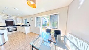 A modern kitchen with a central island, built-in oven, and a dining area with a glass table. - Stunning Coastal Cottage - Sleeping 4 in 2 Bedrooms - Pool and Beach Access Included. (Green Close - Near the Front Field)